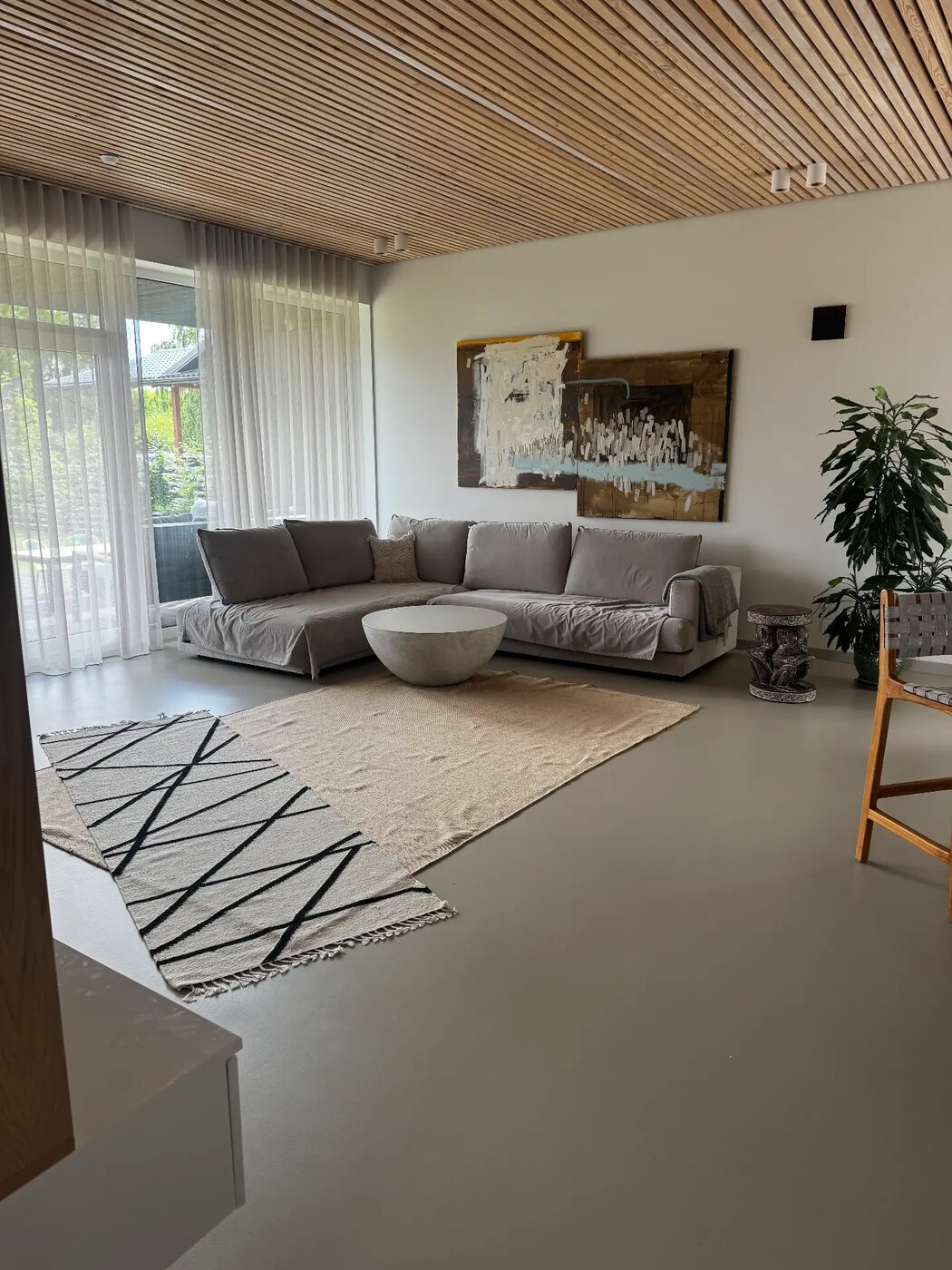 Atviro plano svetainė prieš kuravimą su dviem nedideliais persidengiančiais kilimais ir pilka sofa